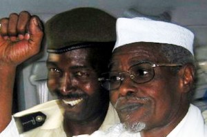 L'ancien président tchadien Hissène Habré lève le poing en signe de victoire alors qu'il quitte un tribunal de Dakar, escorté par un policier sénégalais le 18 novembre 2005