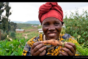 Dans une région du Rwanda, une femme montre fièrement une carotte qu'elle a cultivée dans ses jardins après avoir participé à un project financé par l'ACDI