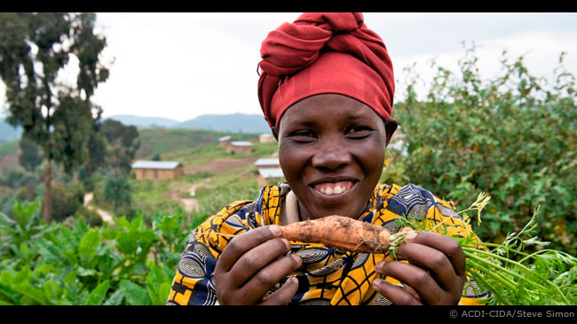 Dans une région du Rwanda, une femme montre fièrement une carotte qu'elle a cultivée dans ses jardins après avoir participé à un project financé par l'ACDI